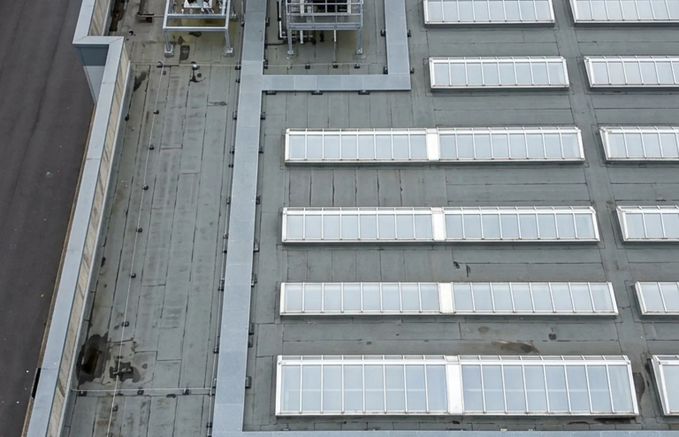 A flat commercial roof photographed straight down, showing rooflights, plant units and water standing around a blocked rainwater outlet