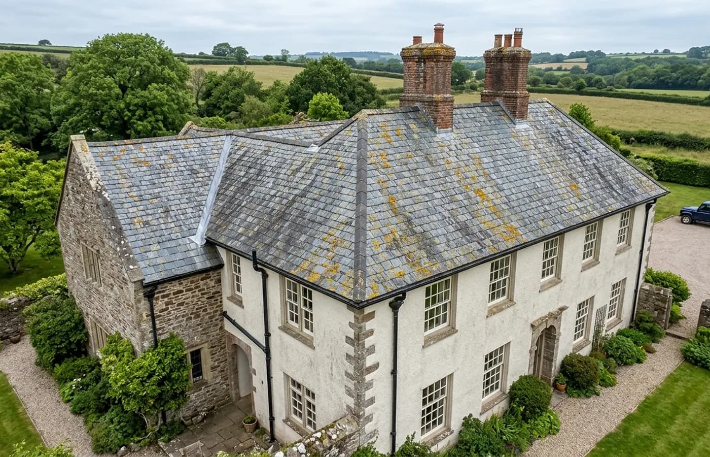 A Devon stone house with a steep natural slate roof photographed from the air, showing the ridge, two brick chimney stacks and a lead lined valley